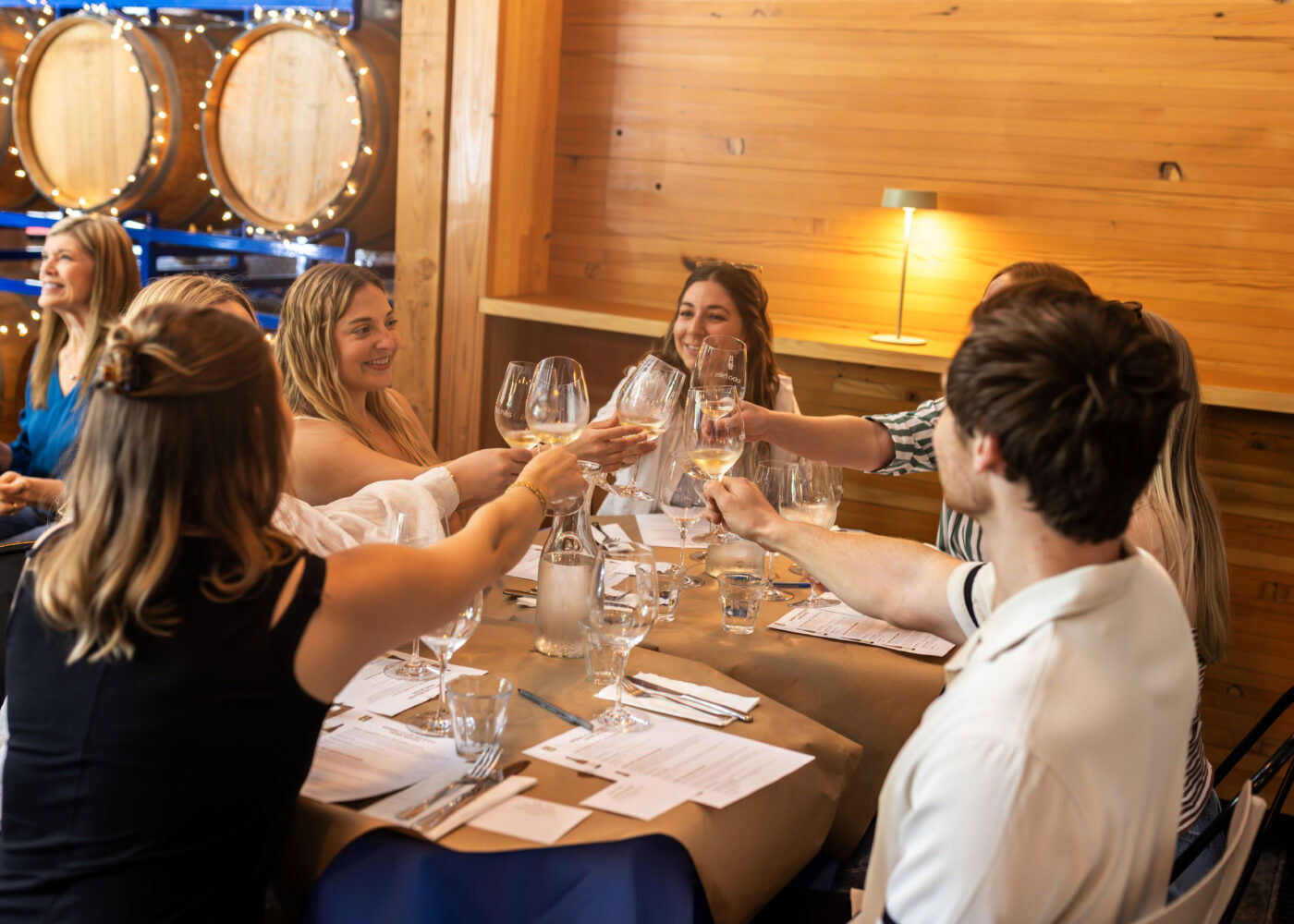 Group of friends enjoying wine tasting at Lobo Hills Wine Co. in a cozy winery setting with wine barrels in the background.