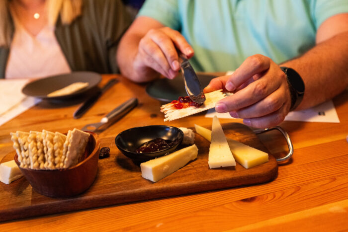 Depict image accurately for accessibility. Man spreading jam on cheese at Lobo Hills Wine Co. cheese tasting event.